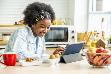 Fototapeta na wymiar Young woman african american in the kitchen while having breakfast and sipping tea or milk in the cup send a message or calls with the tablet and smiles, Concept of social network, message, technology