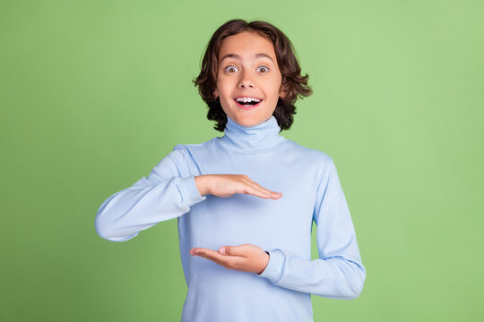 Portrait of attractive cheerful amazed boy holding in hands invisible copy space isolated over bright green color background - Powered by Adobe