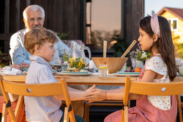 Two kids playing by served table during family dinner against their grandfather
