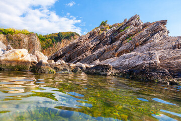 Fototapeta na wymiar Shale coastline and transparent sea water . Idyllic seaside nature with rocks