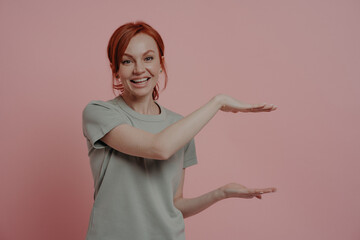 Young pleasant red-haired woman showing huge product size or something big with hands