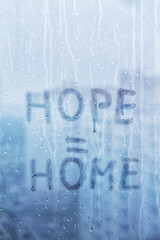 Foggy glass on window with written finger word yellow color Hope is Home concept photo with copy space on blue background