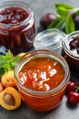 Jars with different jams and fresh fruits on grey table, closeup