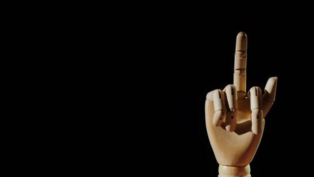Wooden hand shows obscene gesture with middle finger on black background