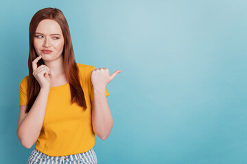 Portrait of unsure adviser lady pointing thumb empty space finger cheek think on blue background