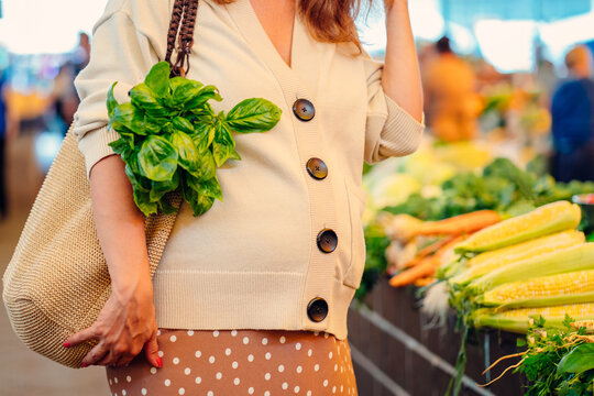 Close up of pregnant woman choosing fresh green and vegetables at street farmer market, outdoor. Sale, shopping, healthy bio food, pregnancy and people concept