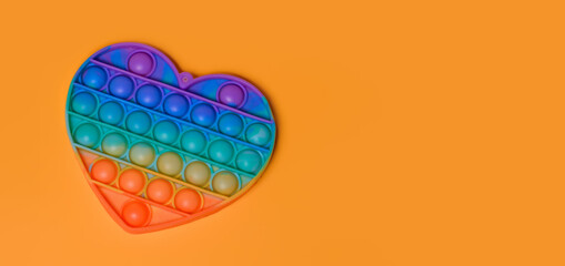 Popit - New popular colorful silicone sensory trendy toy antistress in the form of a heart on an orange background.Rainbow color.Copy space.