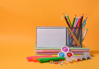 School supplies: notebooks, books, colored pencils, simple dimple - New popular colorful silicone sensory trendy toy antistress on an orange background. Back to school. Copy space. - obrazy, fototapety, plakaty