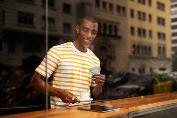 Handsome young african man in cafe drinking coffee. Portrait of happy man with credit card drinking coffee in cafe..