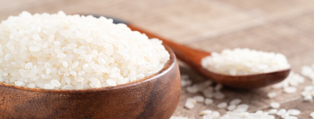 Raw white rice in a wooden bowl over table.