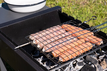 Raw sausages on grill on the charcoal grill, summer picnic in nature, barbecue bbq grill traditional German bratwurst hot dogs 