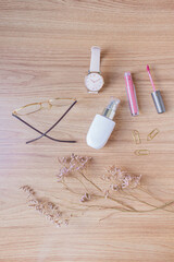 Beauty blog fashion concept. Female styled accessories: glasses, foundation, paper clips, wrist watch, lipstick on wooden background. Flat lay, top view trendy feminine background.