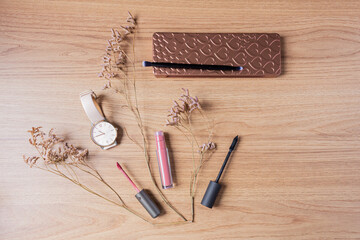Fototapeta na wymiar Beauty blog fashion concept. Female styled accessories: makeup, watch, foundation, watch, mascara, lipstick and dried flower on wooden background. Flat lay, top view trendy feminine background.