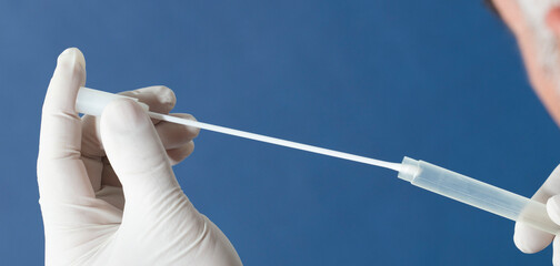 mouth swab in the hands of a doctor or nurse wearing white surgical gloves, inserted into a transporter vial, with a blue background