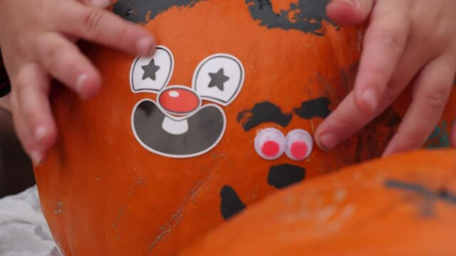 Close-up shot of a child showing a pumpkin decorated with stickers, googly. Close up video of a pumpkin decorated with stickers, googly eyes and paint.