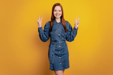 Portrait of lovely pretty positive lady raise hands show two v-signs on yellow background