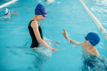 A group of boys and girls train and learn to swim in the pool with an instructor. Development of children's sports.