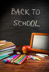 Pile of book and exercise books with shool applies and apple snack with chalkboard.