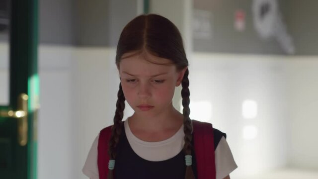 Slider shot of cute upset preteen girl with backpack walking in empty school corridor