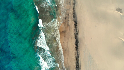 Blue turquoise sea water seen from far above at a golden sand shore.