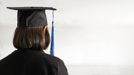 Rear view of a young happy Southeast Asian woman university graduate in graduation gown and...