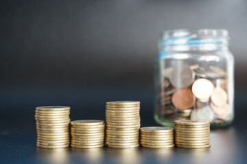Stack of money coin and coin in a glass jar on black background, Saving money concept