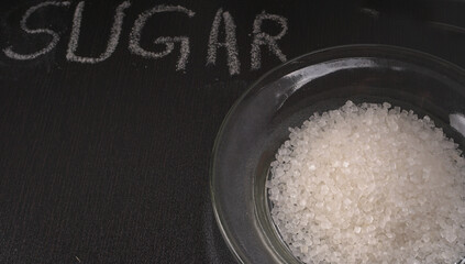 Sugar in glass bowl on wooden background.