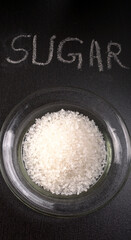 Sugar in glass bowl on wooden background.