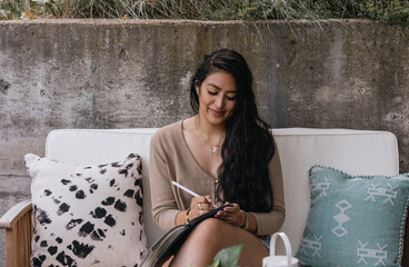 Young adult Filipino woman writing and journaling outdoors at home on patio