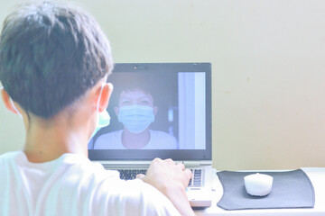 Asian man wearing a mask and video calling his friend on a laptop