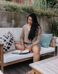 Young adult Filipino woman reading outdoors at home on patio