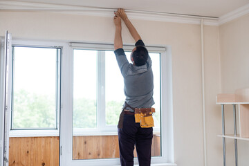 Fototapeta na wymiar A handyman installing new cornice for curtains, home repair and renovation works