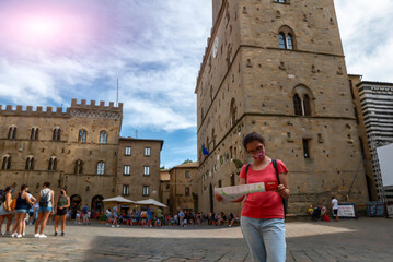 Volterra, Tuscany, Italy. August 2020. In piazza dei priori a middle-aged woman consults the tourist map. She has the mask to defend herself from the coronavirus. Concept of a new normal on vacation.