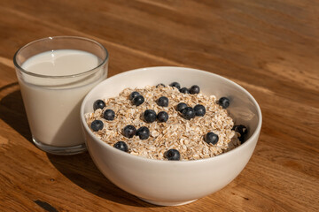 White plate of oatmeal with blueberries and milk on a brown wooden table. Healthy breakfast