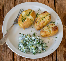 Baked potatoes with cheese and cucumber salad with sour cream on white plate.