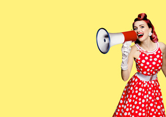 Portrait of red purple haired woman holding mega phone, shout advertising something. Girl in pin up style dress. Isolated on yellow color background with mock up. Female model in retro fashion concept