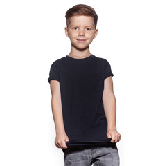 Cool happy little boy wearing blue dark t-shirt and jeans posing, smiling on gray studio...