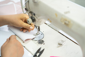 Close up view of sewing process. Female hands stitching white fabric on professional manufacturing machine at workplace. Seamstress hands holding textile for dress production.