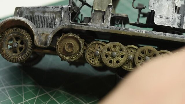 Scale Modeling. Wheels aging and weathering process on the German 8ton Semi Track plastic model. A man creates smudges of dirt on track wheels close-up.