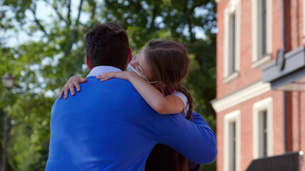 Back view of father in mask squatting meeting daughter from school and hugging