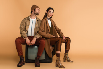 young couple in fashionable autumn outfit sitting on vintage tv set on beige background