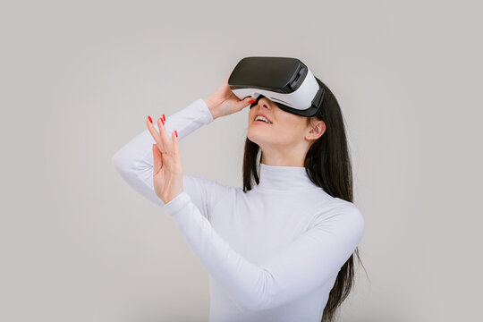 Beautiful woman using VR helmet while touching air on gray background. Girl in glasses of virtual reality. Augmented reality, game, future technology concept. VR.
