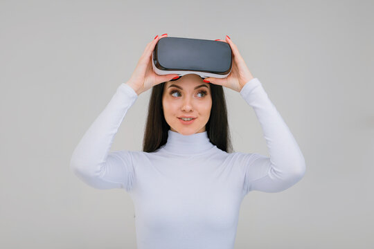 Beautiful woman using VR helmet while touching air on gray background. Girl in glasses of virtual reality. Augmented reality, game, future technology concept. VR.