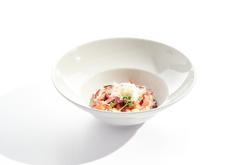 Risotto alla carbonara on white restaurant plate. Risotto with bacon and egg, garnished with micro greens. Risotto topped with parmesan cheese.