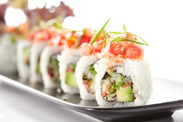 Healthy vegetarian Japanese lunch. Vegan sushi roll with avocado and mushrooms inside. Topped with tomato. Vegetarian sushi rolls dish. Restaurant asian vegan food isolated on white background.