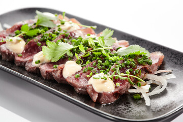 Beef tataki - seared beef,. thinly sliced sashimi style. Beef tataki served with delicious ponzu tataki sauce. Japanese style meat on black plate isolated on white background..
