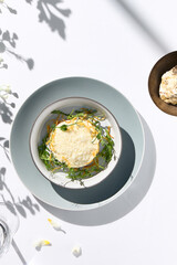 Beef tartare under cheese sauce with deep fried onion. Fancy dinning with beef tartare on white table with simple contemporary decoration. Sunlight and harsh shadow still life. Beef tartare blue dish.