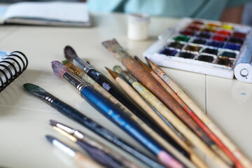 on the table there is a notebook, brushes and watercolor paints