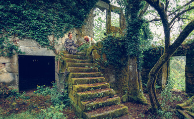 Chica con vestido de flores entrenando a su perro en las escaleras de un entorno mágico. Naturaleza sobre ruinas, perro dando la pata a su entrenadora.
