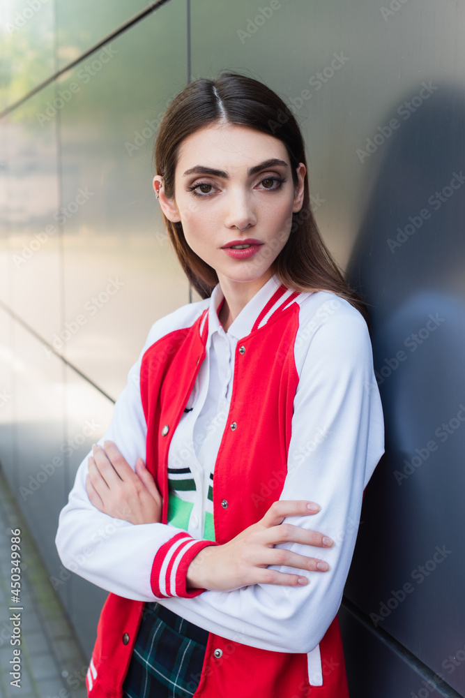 Wall mural stylish woman with crossed arms looking at camera near grey wall